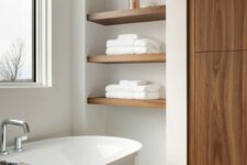 39 a refined contemporary bathroom clad with neutral tiles, a wardrobe, built-in shelves in a niche, an oval tub and a window