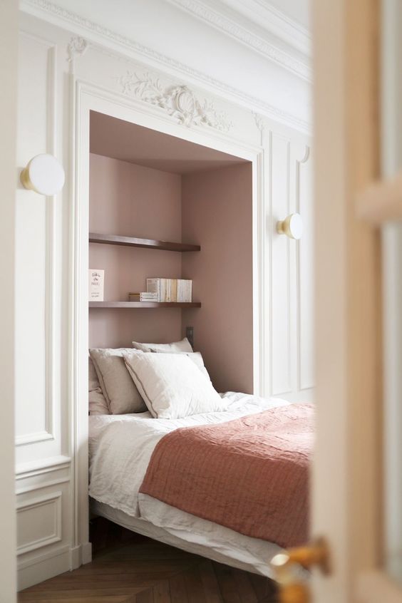 a refined French bedroom with a large niche painted dusty pink, a bed placed in there and some stained shelves and sconces