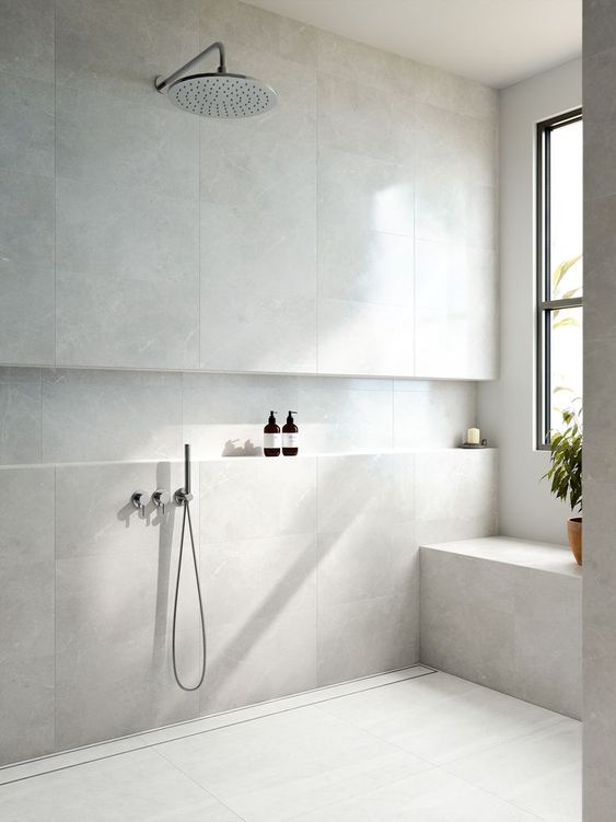 A serene neutral bathroom clad with large scale tiles, with a built in bench and a niche used for storage looks very minimal
