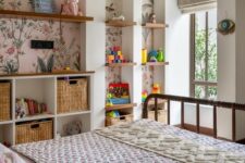 43 a bright kids’ room with a series of arched niches with floral wallpaper, with built-in shelves and baskets, with toys and decor