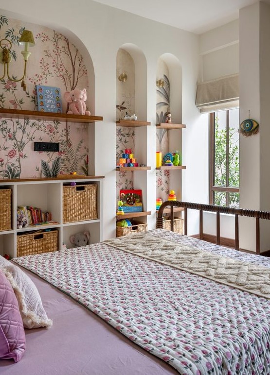 A bright kids' room with a series of arched niches with floral wallpaper, with built in shelves and baskets, with toys and decor