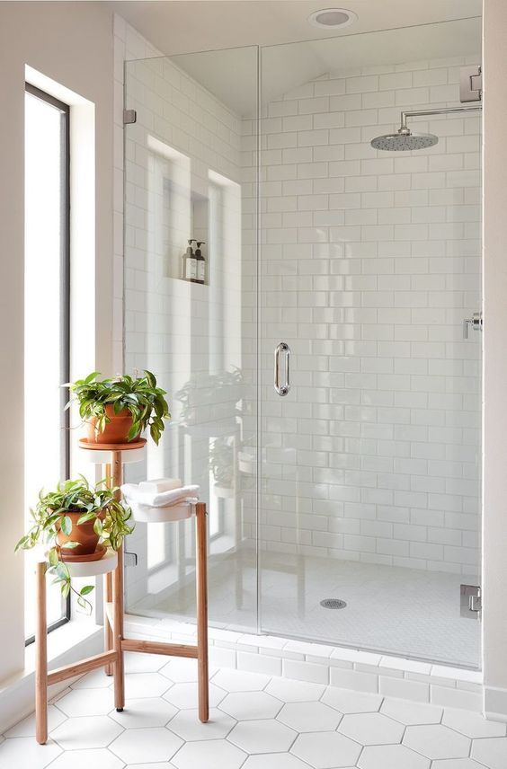 a serene white bathroom clad with hexagon and subway tiles, with a niche for storage, a plant stand with potted greenery