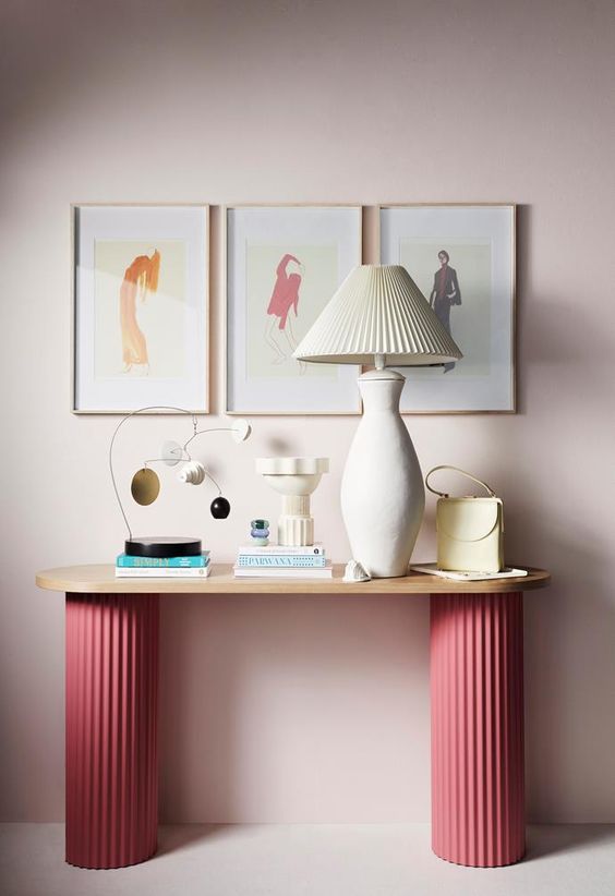 an eye-catching console table with pink fluted legs, a lamp with a fluted lampshade, some deco and a gallery wall