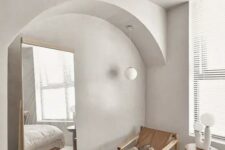 44 a contemporary bedroom in cold neutral tones, with an arched niche with a floor mirror, a wood and leather chair and a lamp