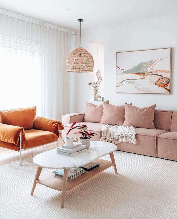 A bright living room with a pink olefin sectional, a rust colored chair, a tiered coffee table and a bold artwork