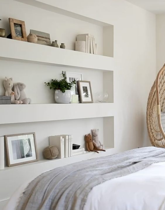 A Scandinavian bedroom with a series of niches with decor and books, a bed with neutral bedding and an egg shaped chair