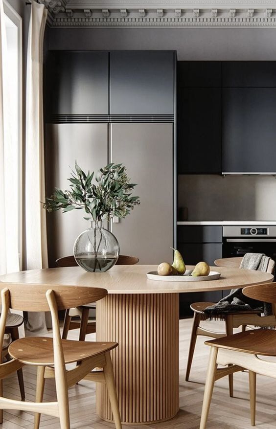 a black kitchen, a round table with a fluted base, light-stained chairs, greenery in a vase are a chic and modern combo