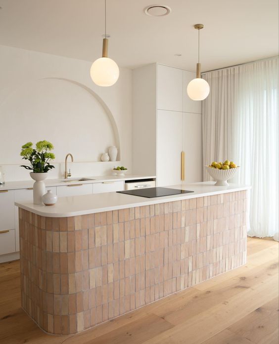 a refined and beautiful kitchen with white cabinets, a terracotta tile kitchen island, an arched niche for decor and pendant lamps