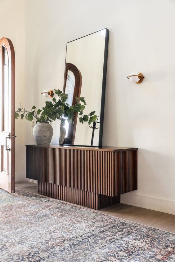 a cool stacked reeded console table with an oversized mirror, a planter with greenery and a sconce is a cool idea