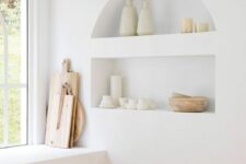 50 a serene white kitchen with lower cabinets, niche shelves used for decor and display and wooden cutting boards is a lovely space