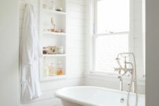 51 a white farmhouse bathroom clad with shiplap, with a niche with shelves and some lovely decor, a clawfoot tub and windows