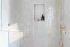 53 a white shower space with Zellige tiles, a niche shelf, gold fixtures and a small shelf or bench in the corner