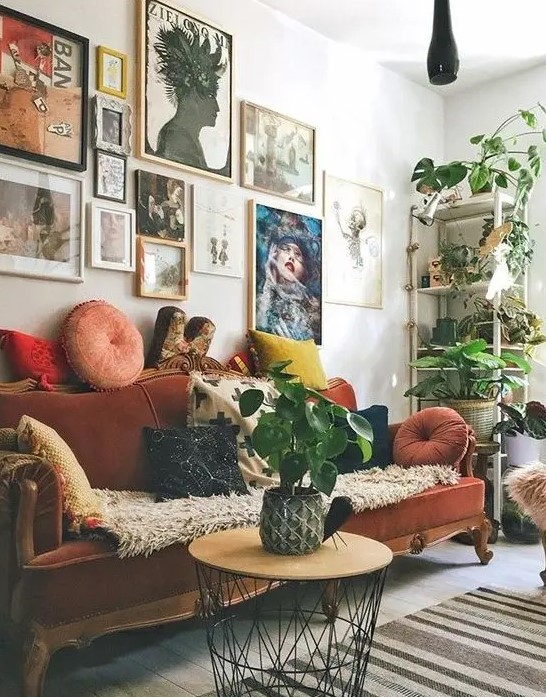 a maximalist living room with a colorful gallery wall, a rust-colored velvet vintage sofa, a round table and potted plants