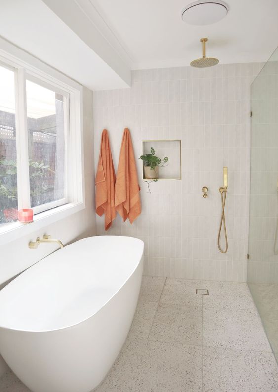 an airy modern bathroom with a shower space, an oval tub, a terrazzo floor, a skinny tile wall and a niche for decor