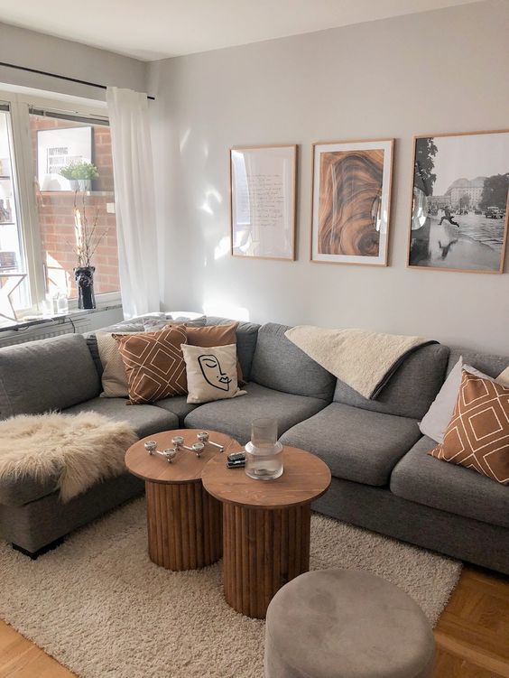 a modern living room with a grey sectional and pillows, a duo of fluted coffee tables, a neutral rug and a gallery wall
