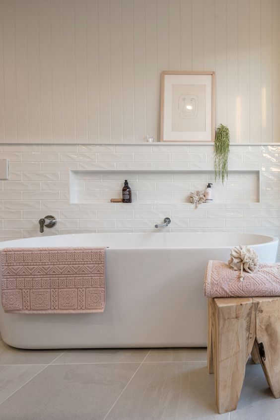 an airy modern bathroom with shiplap and skinny white tiles, an oval tub, a wooden stool and a niche in the tiles for some bathroom stuff