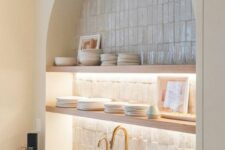 59 an arched niche clad with skinny tiles, open lit up shelves, porcelain and glasses is a decorative and practical idea for a kitchen