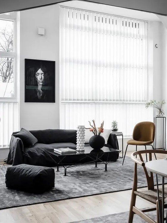 a chic Scandi living room with a black sofa and a pouf, a rust chair and a glass coffee table and some plants