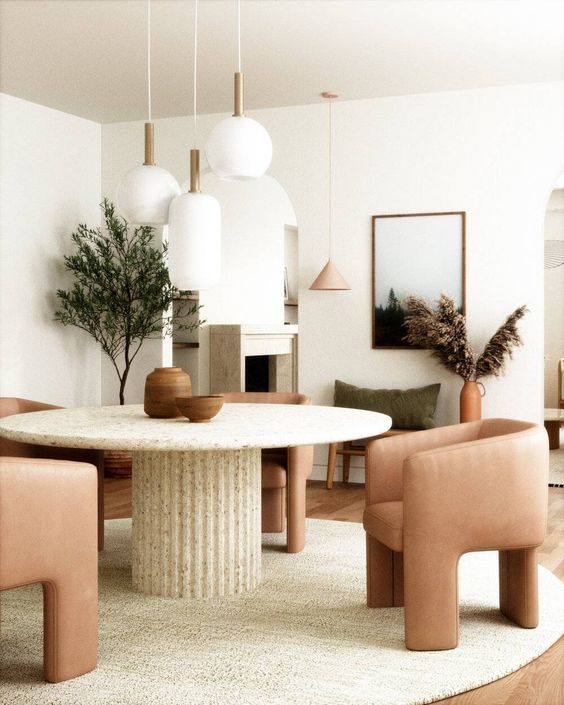 a quirky Japandi dining space with a round table with a fluted base, dusty pink chairs, a cluster of pendant lamps and some grasses