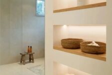 65 a minimalist bathroom with neutral walls, a large shower space enclosed in glass, a series of lit up niche shelves for storage