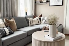 67 a Scandinavian living room with a grey sectional, a fluted coffee table, some decor, printed pillows and neutral curtains