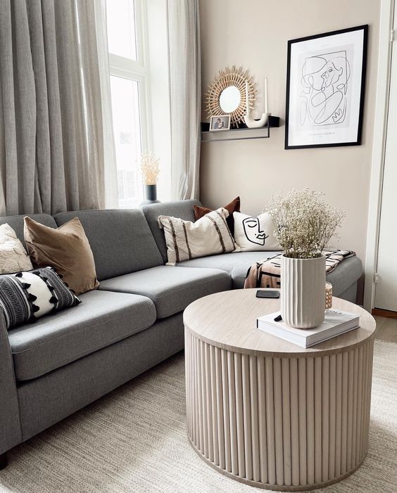 a Scandinavian living room with a grey sectional, a fluted coffee table, some decor, printed pillows and neutral curtains