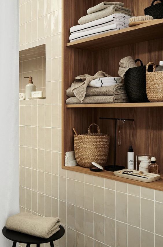 a modern bathroom clad with greige tiles, a ntimber niche with shelves, with decor and some towels is a very chic and cool space