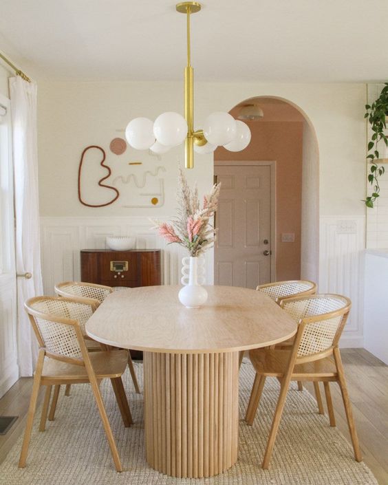 an elegant dining room with a console, a table with a reeded base, cane chairs, a chandelier and some art