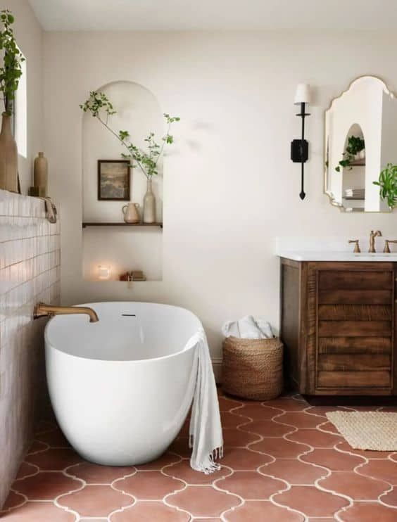 A Mediterranean farmhouse bathroom with a terracotta tile floor, a dark stained vanity, an oval tub, niche shelves and some greenery