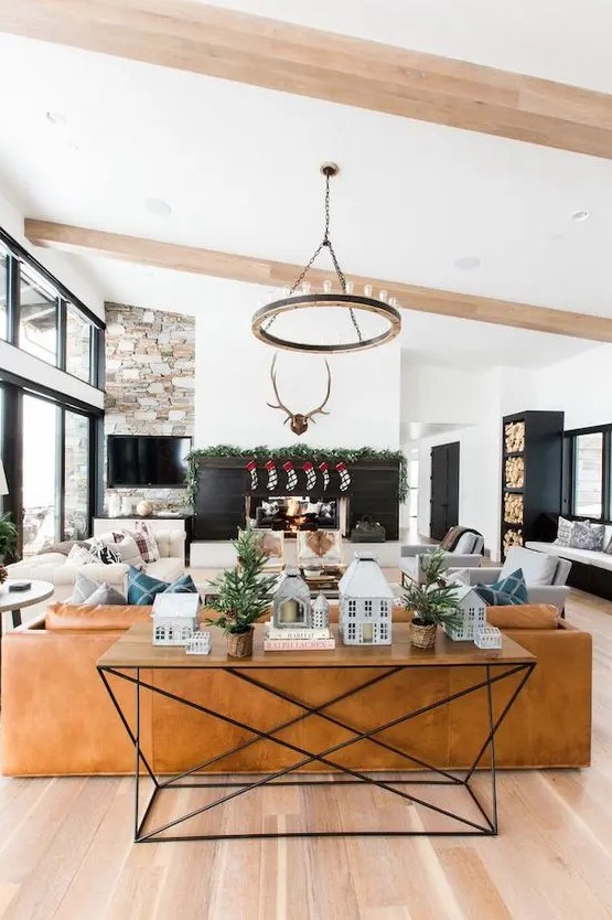 a barn living room with a fireplace clad with black planks, a TV on a stone wall, a leather sofa and neutral seating furniture, a round chandelier
