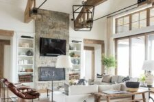 a barn living room with wooden beams, white planked walls, a fireplace clad with stone, neutral seating furniture, leather chairs and baskets