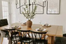 a beautiful and airy modern farmhouse dining room with a gallery wall, a stained table, black chairs, a chandelier and greenery in a vase