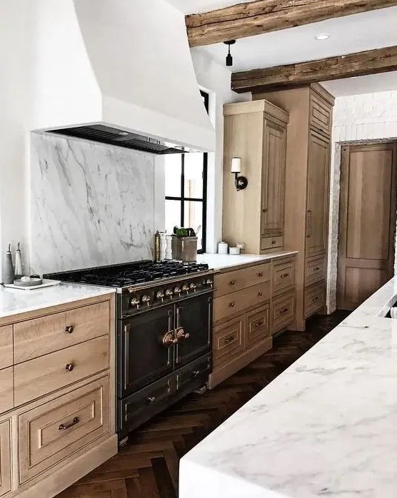 A beautiful and refined kitchen with light stained cabinetry, a white hood and a white marble backsplash plus countertops