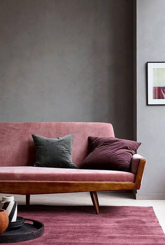 a beautiful and refined living room with grey walls, a pink sofa with jewel tone pillows, a pink rug