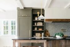 a beautiful farmhouse kitchen with an olive green cabinet and a stained kitchen island, a hood, pendant lamps and gold and brass knobs