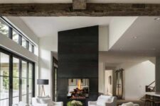 a beautiful modern farmhouse living room with reclaimed wooden beams, a large double-sided fireplace, white seating furniture and a coffee table