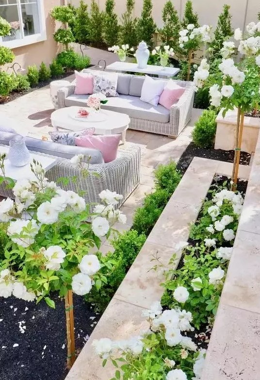 a bright and vivacious outdoor living room done with tiles, white wicker furniture, pastel upholstery and pillows and lots of greenery and blooms