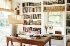 a catchy farmhouse home office with built-in storage units and shelves, a wooden desk and chair, a rustic lamp and woven shades