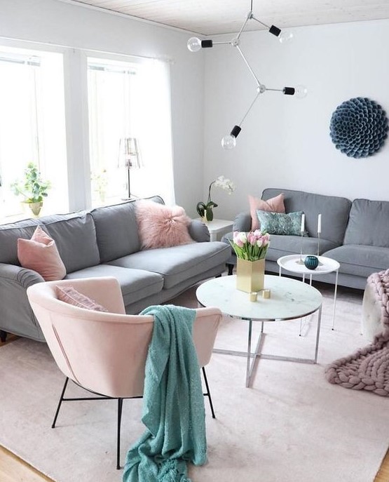 a catchy living room with grey sofas, pink pillows and a chair, coffee tables, a catchy bulb chandelier