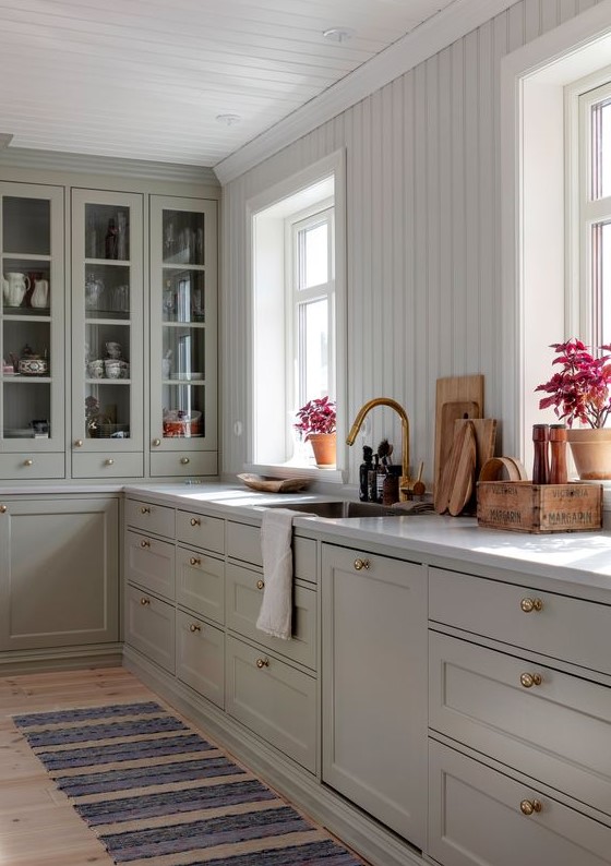 a chic kitchen with grey shaker cabinets and glass ones, a white beadboard backsplash, a white stone countertop