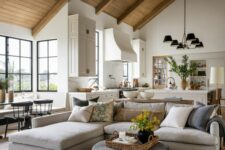 a chic modern farmhouse living room with a neutral sectional, a pouf, a chair, some chandeliers and greenery and blooms
