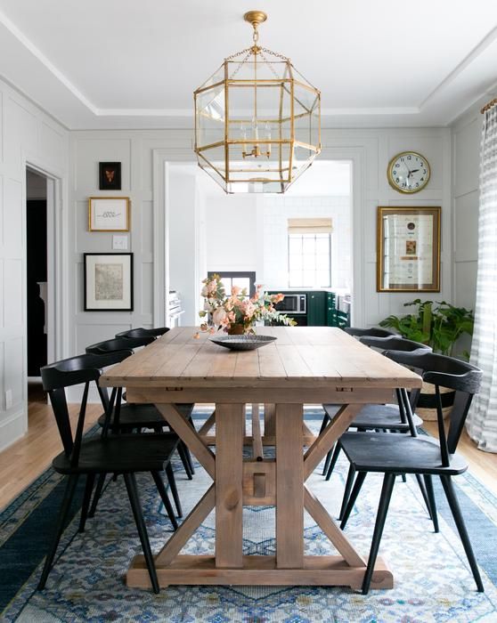 a chic modern farmhouse space with a stained trestle table, black chairs, potted greenery and some artwork, a gold pendant lamp
