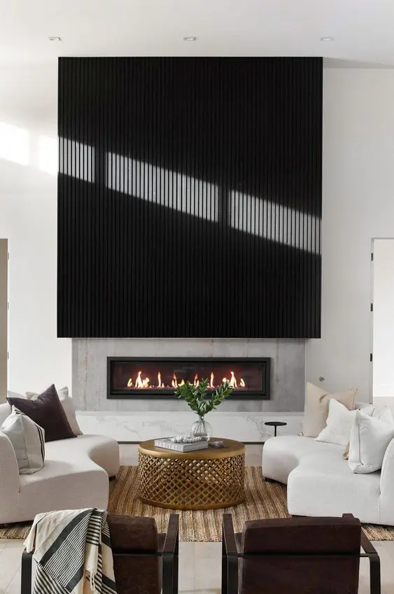 a chic modern living room with a fireplace with a black reeded surround, creamy sofas, brown chairs, a brass coffee table