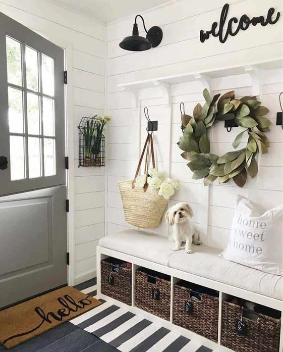 A chic neutral space with a leaf wreath, layered rugs, a built in bench with baskets and some signs