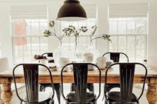 a classy modern farmhouse dining room with a stained table, black metal chairs and a pendant lamp and some greenery