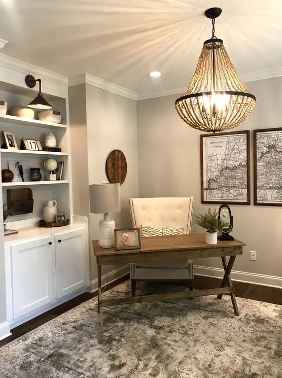 a clean and simple modern country home office with grey walls, a white storage unit, a trestle desk, a leather chair and a wooden bead chandelier