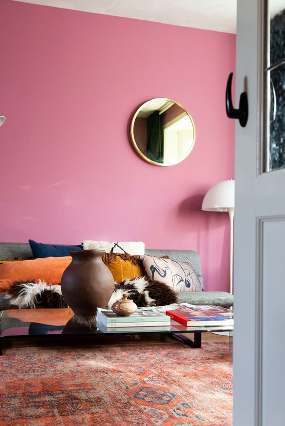 a colorful living room with pink walls, a grey sofa with printed pillows, a low coffee table and a printed rug