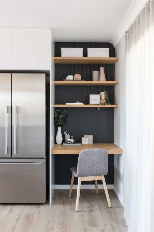 A contemporary farmhouse kitchen with white cabinetry and a working space with a black wall and built in shelves and a desk plus a grey chair