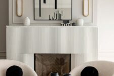 a contemporary space with a fireplace with a reeded surround, an arched mirror, creamy chairs, a black tube chandelier and black pillows