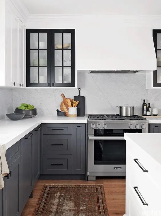 a contrasting kitchen with white upper cabinets and charcoal grey ones, black glass frame cabinets and a white backsplash and countertops